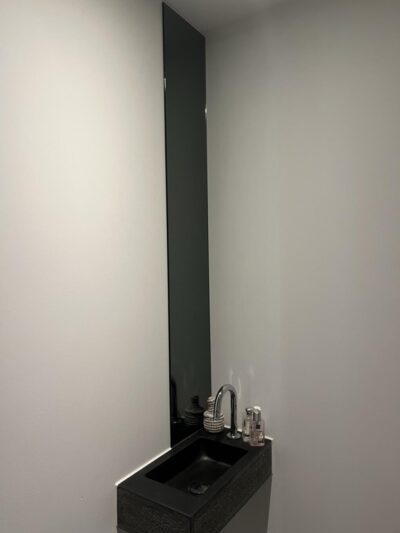 Espejo largo y estrecho encima del lavabo. Pegado en el cuarto de aseo